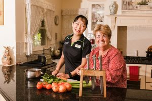 A senior women chopping vegetables. She is pictured with an LCHS staff member. Both are smiling at the camera. 