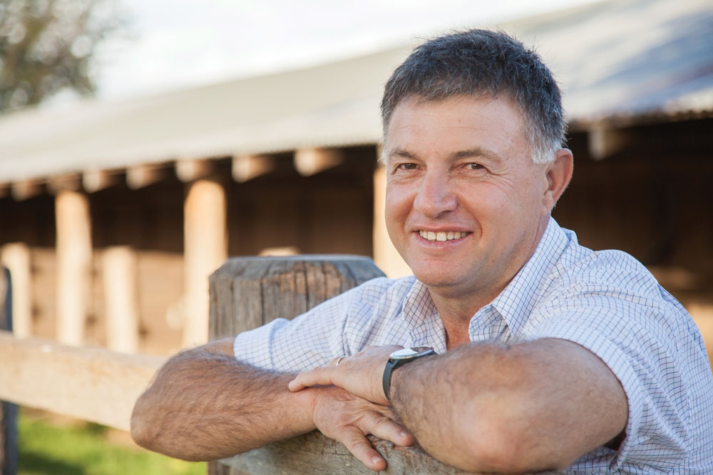 A man leans against a fence post, smiling.