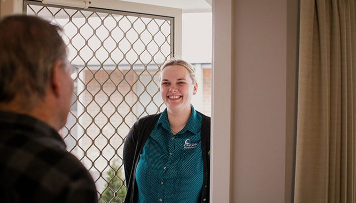 A man opens the door of his home to greet a nurse.